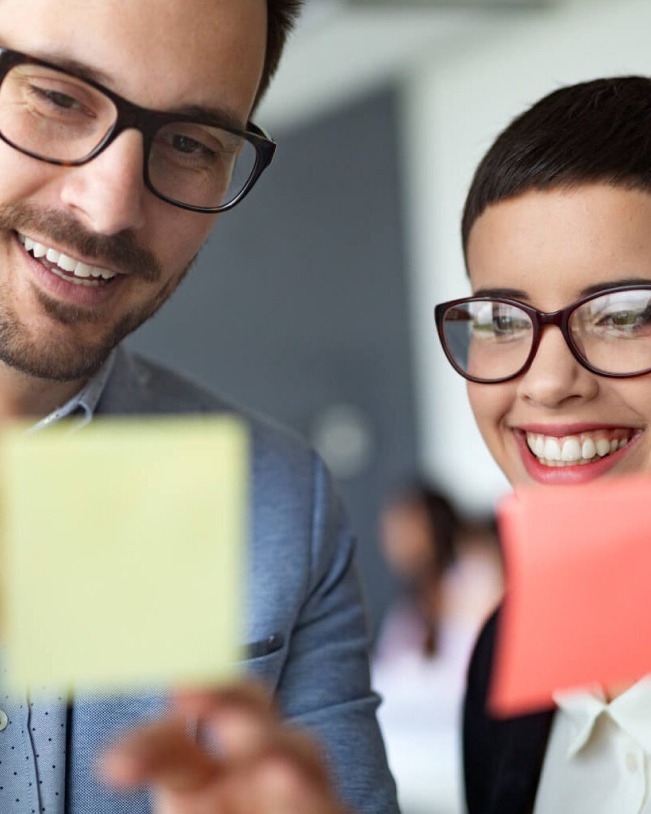 Two people smiling and examining sticky notes.