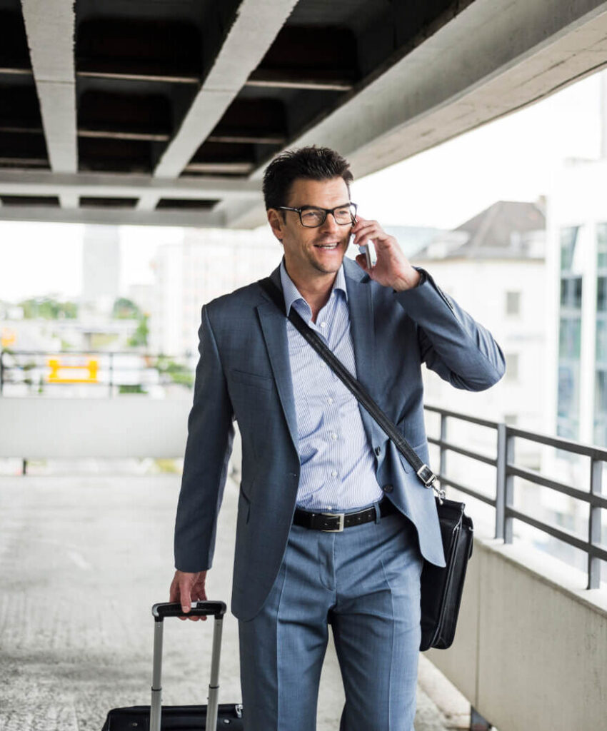 A man in a gray suit and glasses walks while talking on the phone.